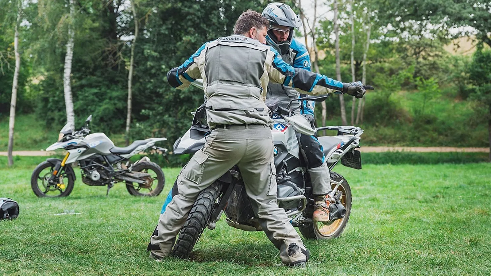 Instruktor motoškoly vede začínající jezdkyni na BMW GS na travnaté ploše