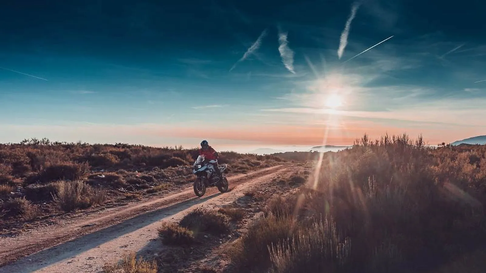 Motorkář na BMW GS na šotolinové cestě ve španělské krajině při západu slunce