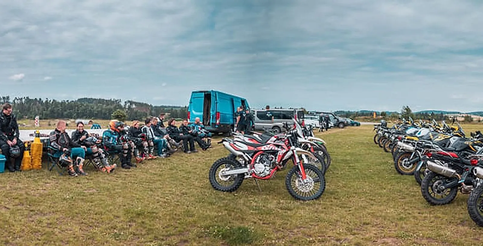 Účastníci týdenního kempu odpočívají u zaparkovaných endur a motorek BMW GS na louce