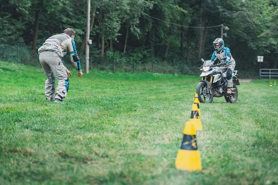 Instruktor motoškoly učí jezdce na BMW GS mezi kužely na travnaté ploše